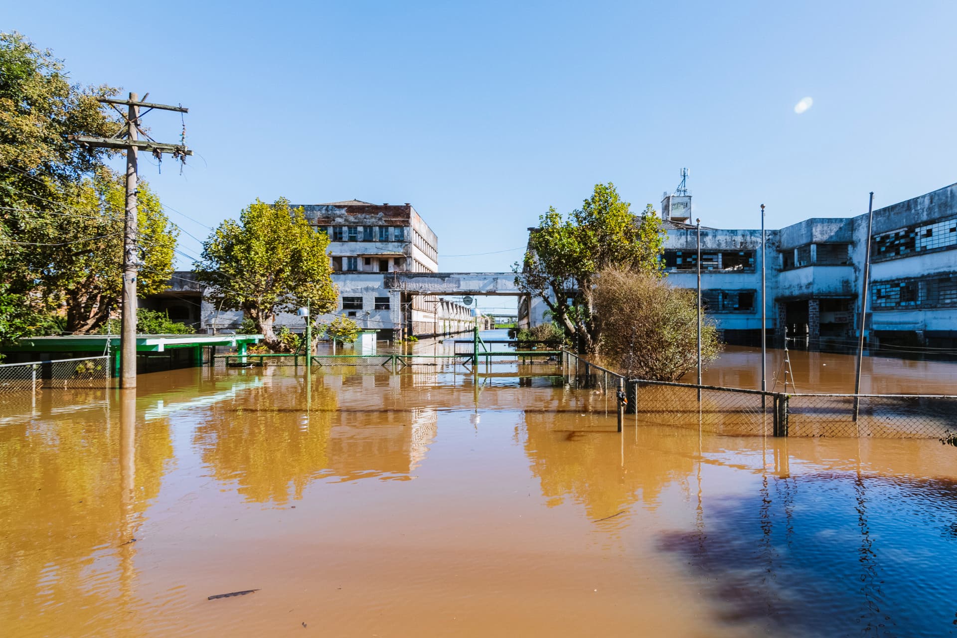 Fábrica Guahyba alagada durante a enchente, com água marrom cobrindo o pátio